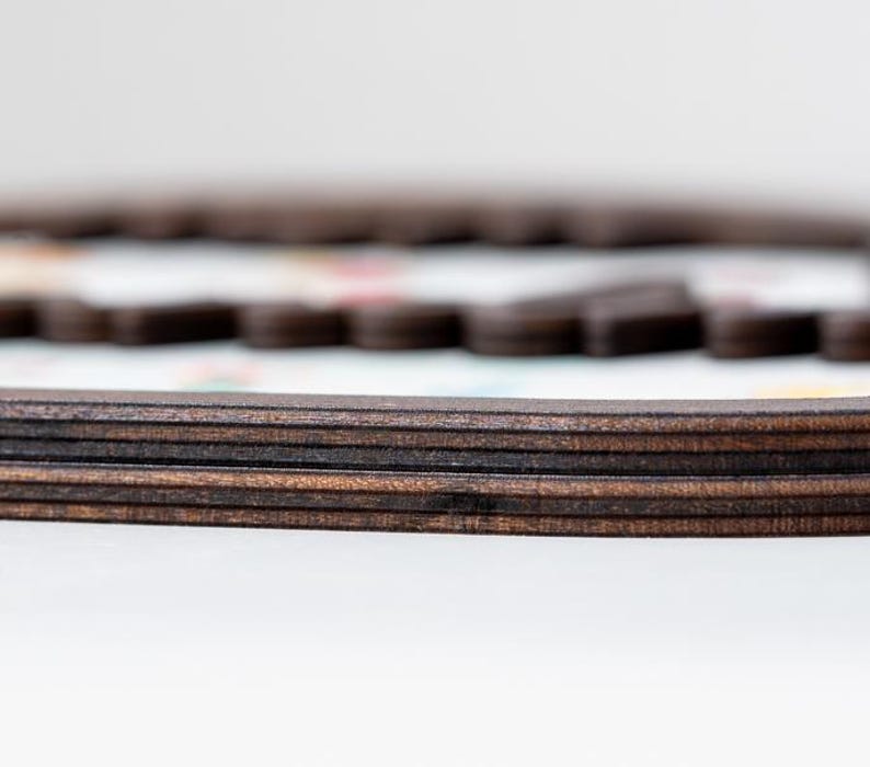Puede incluir: Un marco de madera marr&oacute;n oscuro con una construcci&oacute;n de bordes superpuestos. El marco presenta un acabado liso y pulido con capas de veta de madera visibles en el lateral. Una superficie blanca con patrones coloridos borrosos es visible dentro.