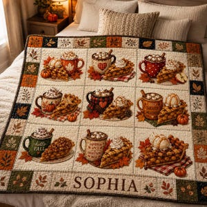 Op de afbeelding: Een quilt met een raster van negen vierkanten, elk met een mok warme drank en een stuk taart. De mokken bevatten teksten zoals 'COZY SWEATER WEATHER', 'hello FALL' en 'PUMPKIN SPICE EVERYTHING NICE'. De naam 'SOPHIA' staat onderaan gedrukt.