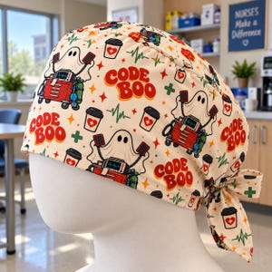 May include: A cream-colored scrub cap featuring a repeating pattern of ghosts, red medical crash carts, coffee cups with heart icons, and green EKG lines. The text "CODE BOO" is printed in red letters throughout the fabric design.