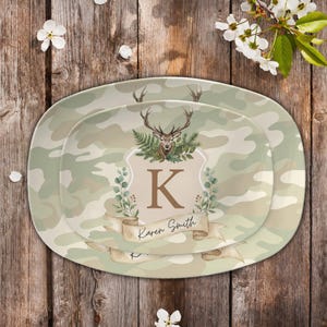 May include: Two oval-shaped serving platters with a camouflage pattern. The platters feature a deer head, the letter "K", and the name "Karen Smith" on a banner. The design includes green foliage and a neutral color palette.