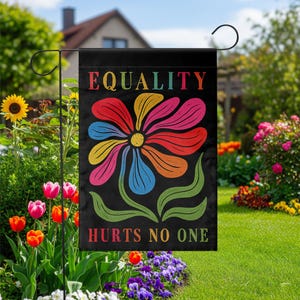Może przedstawiać: Czarna flaga ogrodowa z napisem "EQUALITY HURTS NO ONE" w tęczowych kolorach. Duży, kolorowy kwiatowy wzór jest umieszczony na środku flagi. Flaga jest prezentowana w ogrodzie z kwiatami i zielenią.