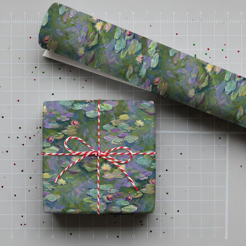 May include: A wrapped gift and a roll of wrapping paper featuring a water lily design in shades of green, blue, and yellow. The gift is tied with red and white twine. The background is a gray grid.
