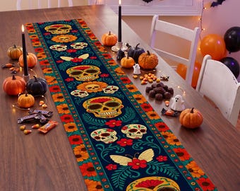Puede incluir: Un camino de mesa rectangular largo con un fondo azul oscuro y un patrón repetitivo de calaveras de azúcar coloridas, flores de cempasúchil naranjas, follaje verde y mariposas color crema. El borde presenta motivos florales en naranja y rojo.