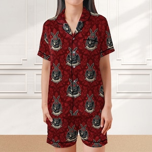 May include: Red pajama set with a repeating pattern of black rabbit illustrations on a damask background. The short-sleeved top and shorts are trimmed with black piping. The rabbit illustrations have red eyes.