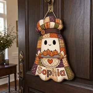 May include: A hanging wall sign shaped like a ghost wearing a chef hat, featuring a patchwork pattern in orange, brown, and purple. The ghost holds a tray of four small pumpkins and has the name Sophia printed in large letters at the bottom.