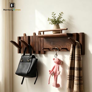 Könnte beinhalten: Ein dunkelbrauner Wandgarderobenständer aus Holz mit mehreren Haken und einem kleinen Regal. Eine schwarze Handtasche, ein rosa Plüschtier und ein karierter Schal hängen an den Haken. Eine kleine Pflanze in einem braunen Topf steht auf dem Regal. Der Text "Harmony Homes" ist sichtbar.