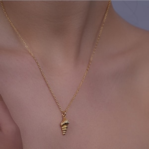 Könnte beinhalten: Eine goldfarbene Halskette mit einem Muschel-Anhänger. Der Anhänger ist eine detaillierte Miniatur einer Muschel. Die Halskette ist zierlich und hängt am Hals einer Person.