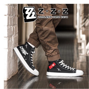 Puede incluir: Zapatillas de lona negras de caña alta con costuras blancas y una estrella blanca en el lateral. La zapatilla izquierda tiene la palabra "SHARKS" escrita en blanco en el lateral. La zapatilla derecha tiene un parche rojo con un diseño de espina de pescado. Las zapatillas las lleva puestas una persona que lleva pantalones marrones. El texto "Z.Z.Z. zenless zone zero" es visible por encima de la cabeza de la persona.