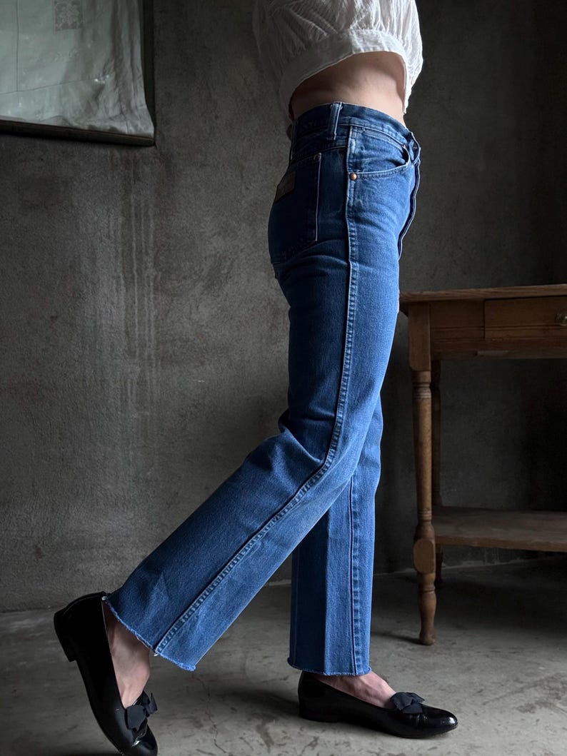 May include: Blue denim jeans with a straight leg and a classic five-pocket design. The jeans are worn with black leather loafers. The jeans have a dark wash and a slight flare at the hem.