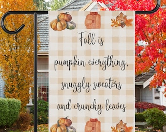 Puede incluir: Bandera de jardín con temática otoñal con fondo a cuadros. La bandera presenta una ilustración de acuarela de calabazas, un suéter y hojas. El texto en la bandera dice "Fall is pumpkin everything, snuggly sweaters and crunchy leaves."