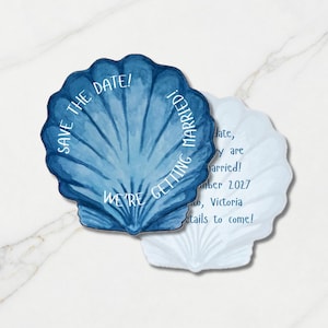 Op de afbeelding: Twee schelpvormige kaarten met aquarelblauwe ontwerpen. De bovenste kaart bevat de tekst SAVE THE DATE! WE'RE GETTING MARRIED! De onderste kaart toont tekst inclusief de datum september 2027 en de locatie Victoria, met details.