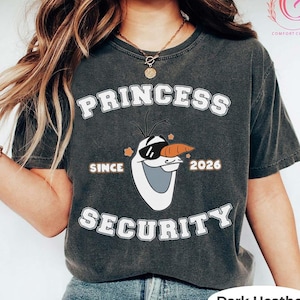 以下が含まれることがあります： 「PRINCESS SECURITY SINCE 2026」の文字と、サングラスをかけたアナと雪の女王のオラフのグラフィックがプリントされたダークヘザーグレーのTシャツ。Comfort Colorsブランドです。