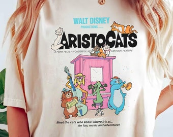 May include: A white t-shirt with a vintage-style graphic of the Disney movie "The Aristocats". The graphic features the title of the movie, the Walt Disney Productions logo, and a scene of the cats from the movie playing music.