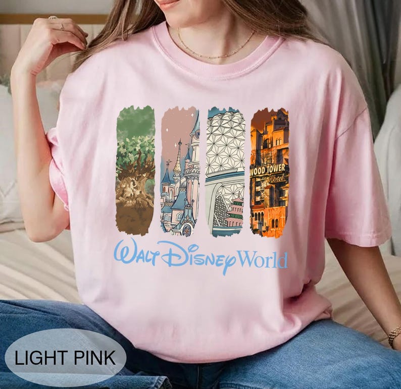 May include: Light pink t-shirt with a Walt Disney World graphic. The design features four vertical rectangular images with illustrations of the Tree of Life, a castle, a geometric structure, and the Tower of Terror. The words "Walt Disney World" are written in light blue.