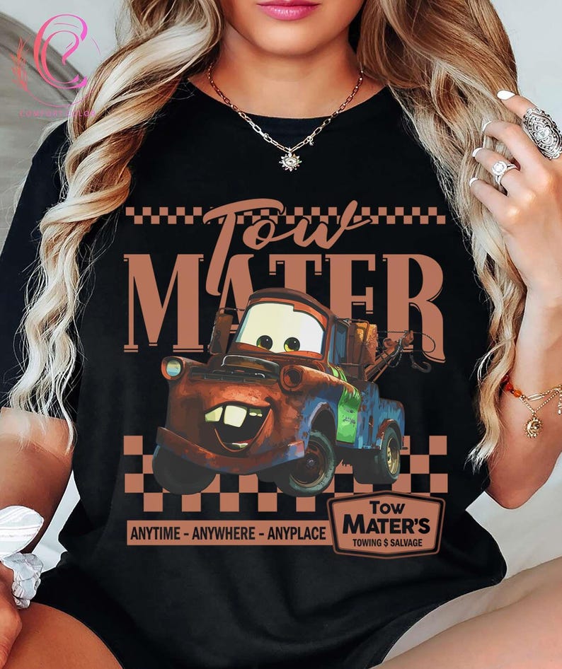 Puede incluir: Camiseta negra con una imagen de dibujos animados de Mate de la pel&iacute;cula Cars. El dise&ntilde;o incluye el texto "Tow Mater" encima del personaje y "ANYTIME - ANYWHERE - ANYPLACE" debajo. Un peque&ntilde;o letrero dice "Tow Mater's Towing & Salvage."