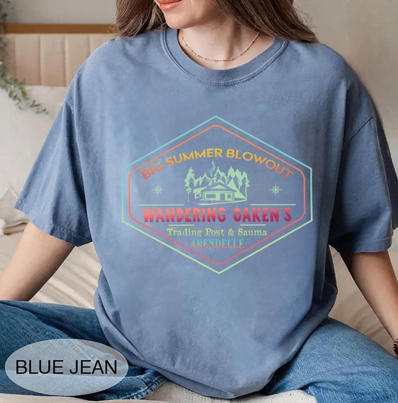 May include: A blue jean colored t-shirt with a graphic that reads "Big Summer Blowout, Wandering Oaken's Trading Post & Sauna, Arendelle." The graphic is a multi-colored hexagon with a cabin and trees.