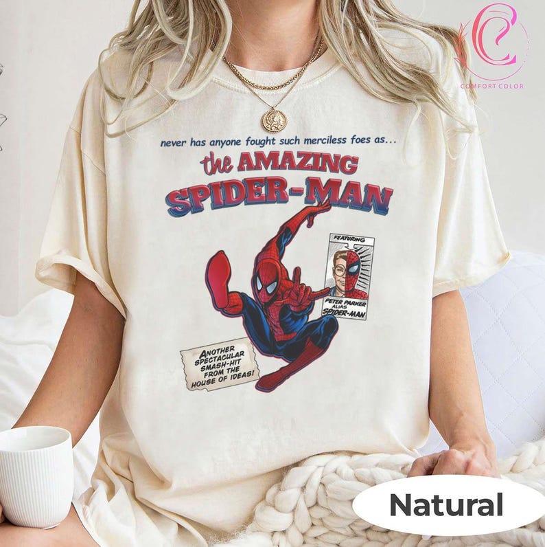 Op de afbeelding: Cr&egrave;mekleurig T-shirt met een stripboekafbeelding van Spider-Man in rood en blauw. Het shirt heeft de tekst "the AMAZING SPIDER-MAN" en andere stripboekelementen. Het shirt is onderaan voorzien van het label "Natural".