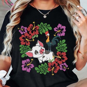 Może przedstawiać: Czarny t-shirt z kolorową grafiką świni, koguta, kwiat&oacute;w hibiskusa i zielonych liści. Świnia jest biała z czarnymi plamami i r&oacute;żowymi uszami. Kogut jest czerwony, ż&oacute;łty i niebieski. Kwiaty są czerwone i fioletowe.