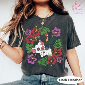 Może przedstawiać: Ciemnoszara koszulka z nadrukiem świni i koguta z kresk&oacute;wki, otoczonych czerwonymi i fioletowymi kwiatami hibiskusa i zielonymi liśćmi. Na dole znajduje się napis "Dark Heather".