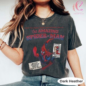 Op de afbeelding: Donker heather t-shirt met The Amazing Spider-Man. De afbeelding toont het personage in actie, de comic-titel en een paneel met Peter Parker. Het shirt heeft ook de tekst "Another Spectacular Smash-Hit From The House of Ideas!"