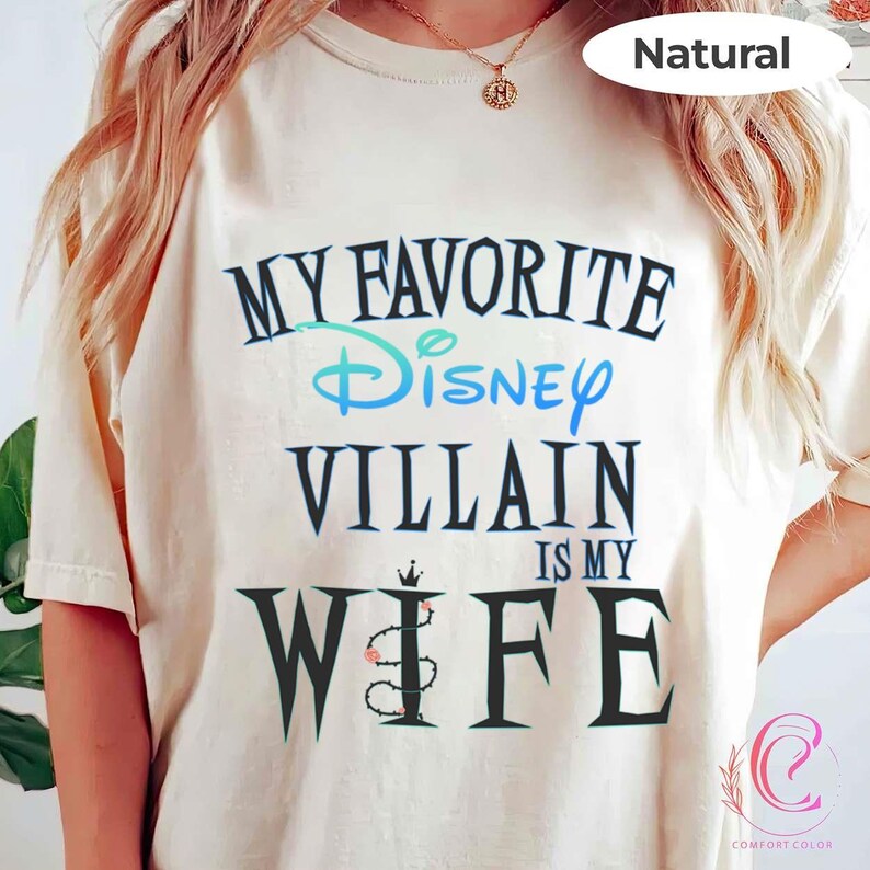 Peut inclure: T-shirt cr&egrave;me avec l'inscription "MY FAVORITE Disney VILLAIN IS MY WIFE" en noir et bleu sarcelle. Le mot "Disney" est &eacute;crit en script. Le t-shirt a une coupe d&eacute;contract&eacute;e et des manches courtes.
