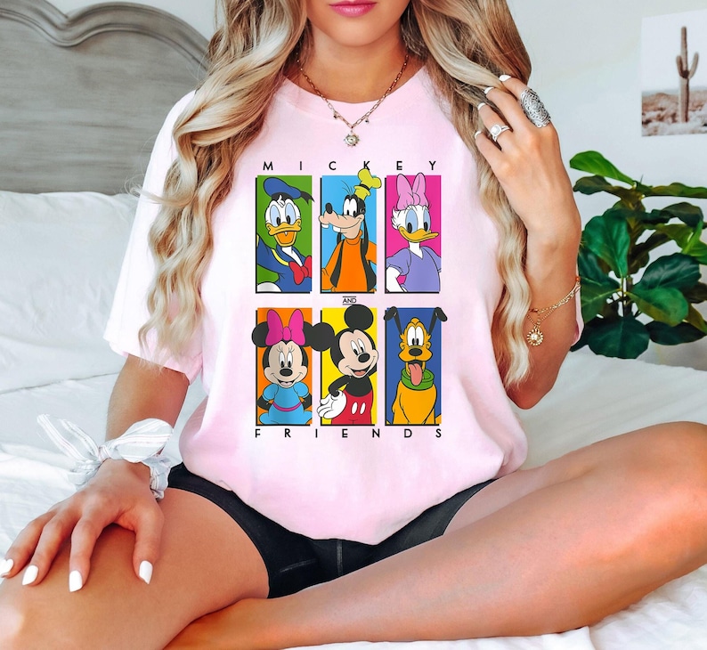 May include: Pink t-shirt with a graphic print of Mickey Mouse and his friends. The text "Mickey and Friends" is printed below the graphic.