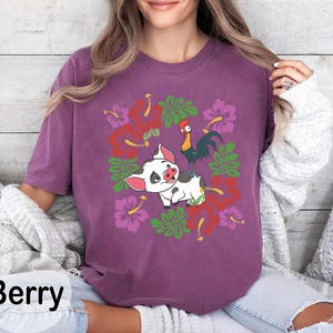 Może przedstawiać: Koszulka w kolorze jagodowym z kresk&oacute;wkową świnią i kogutem z kwiatowymi akcentami. Koszulka ma okrągły dekolt i kr&oacute;tkie rękawy. Słowo "Berry" jest wydrukowane w lewym dolnym rogu obrazu.