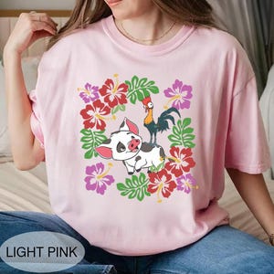 Może przedstawiać: Jasnor&oacute;żowa koszulka z kresk&oacute;wkowym świnią i kogutem otoczonym wieńcem kwiatowym z czerwonych, r&oacute;żowych i fioletowych kwiat&oacute;w hibiskusa i zielonych liści. Tekst "LIGHT PINK" znajduje się na dole.