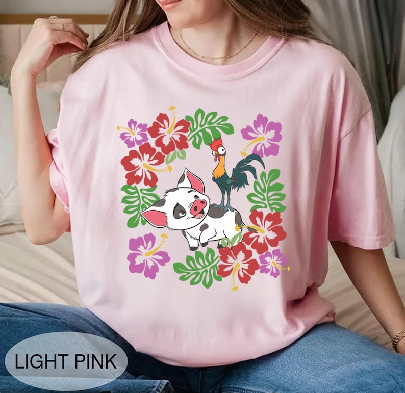 Może przedstawiać: Jasnor&oacute;żowa koszulka z kresk&oacute;wkowym świnią i kogutem otoczonym wieńcem kwiatowym z czerwonych, r&oacute;żowych i fioletowych kwiat&oacute;w hibiskusa i zielonych liści. Tekst "LIGHT PINK" znajduje się na dole.