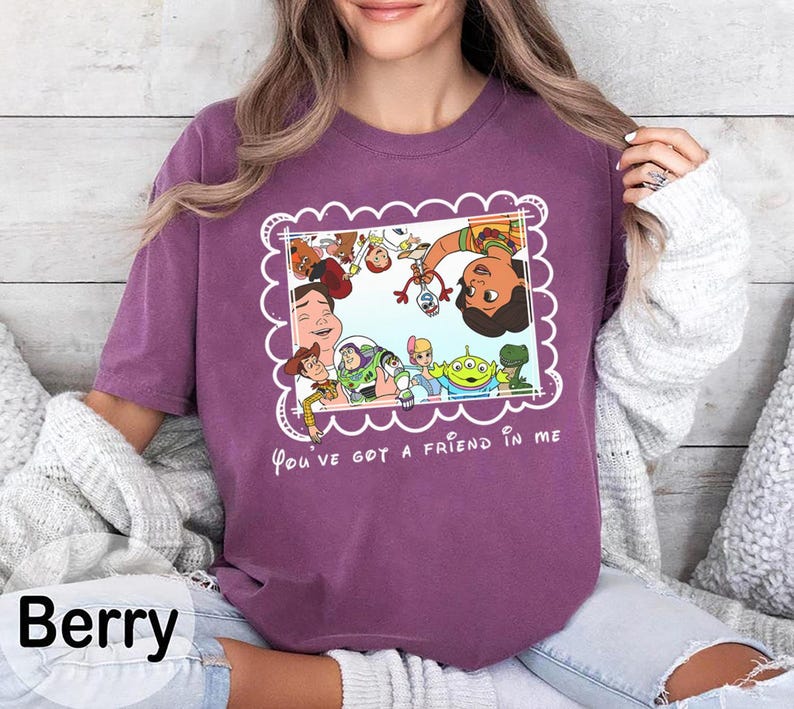 K&ouml;nnte beinhalten: Beerenfarbenes T-Shirt mit einem gerahmten Grafikmotiv von Toy Story-Charakteren, darunter Woody und Buzz Lightyear. Der Text "You've got a friend in me" steht darunter. Das T-Shirt hat einen Rundhalsausschnitt.