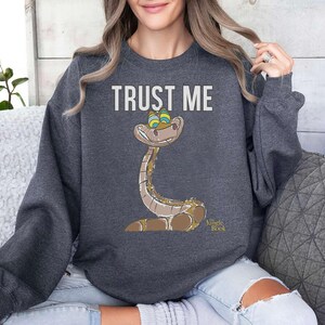May include: A dark gray sweatshirt with the text "TRUST ME" and a cartoon image of a snake from the Jungle Book. The snake is green and brown with yellow eyes.
