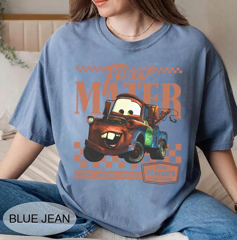 Puede incluir: Camiseta azul claro con un dise&ntilde;o de Mate de la pel&iacute;cula Cars. El dise&ntilde;o incluye el texto "Tow Mater" en naranja, con una imagen de dibujos animados del personaje. La camiseta tambi&eacute;n tiene el texto "Blue Jean" en la parte inferior.