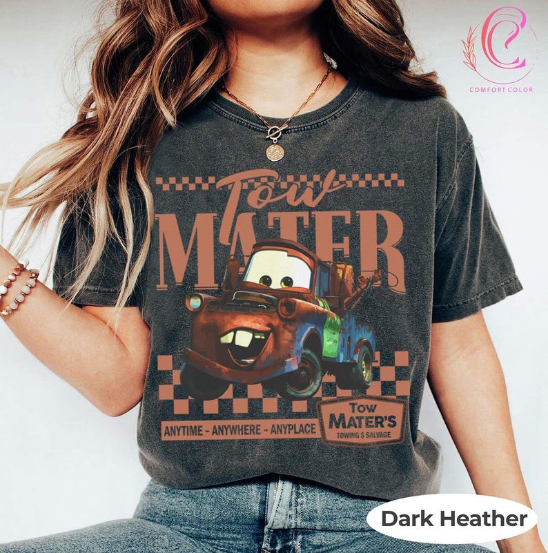 Puede incluir: Camiseta gris oscuro jaspeado con un gr&aacute;fico de Mate de la pel&iacute;cula Cars. El dise&ntilde;o incluye el texto "Tow Mater" y "Tow Mater's Towing & Salvage". La camiseta es de la marca Comfort Colors.