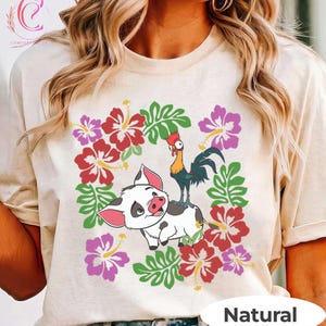 Może przedstawiać: Beżowa koszulka z kolorową grafiką przedstawiającą świnię i koguta otoczone czerwonymi, r&oacute;żowymi i fioletowymi kwiatami oraz zielonymi liśćmi. Słowo "Natural" jest wydrukowane na dole.