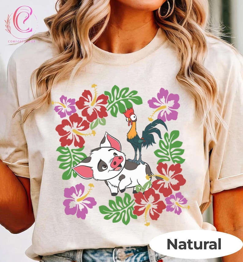 Może przedstawiać: Beżowa koszulka z kolorową grafiką przedstawiającą świnię i koguta otoczone czerwonymi, r&oacute;żowymi i fioletowymi kwiatami oraz zielonymi liśćmi. Słowo "Natural" jest wydrukowane na dole.