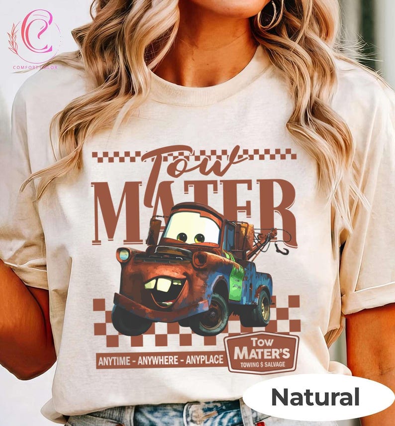 Puede incluir: Una camiseta de color natural con un gr&aacute;fico de Mate de la pel&iacute;cula Cars. El dise&ntilde;o incluye el texto "Tow Mater" en marr&oacute;n, con la imagen de Mate y la frase "Anytime - Anywhere - Anyplace".