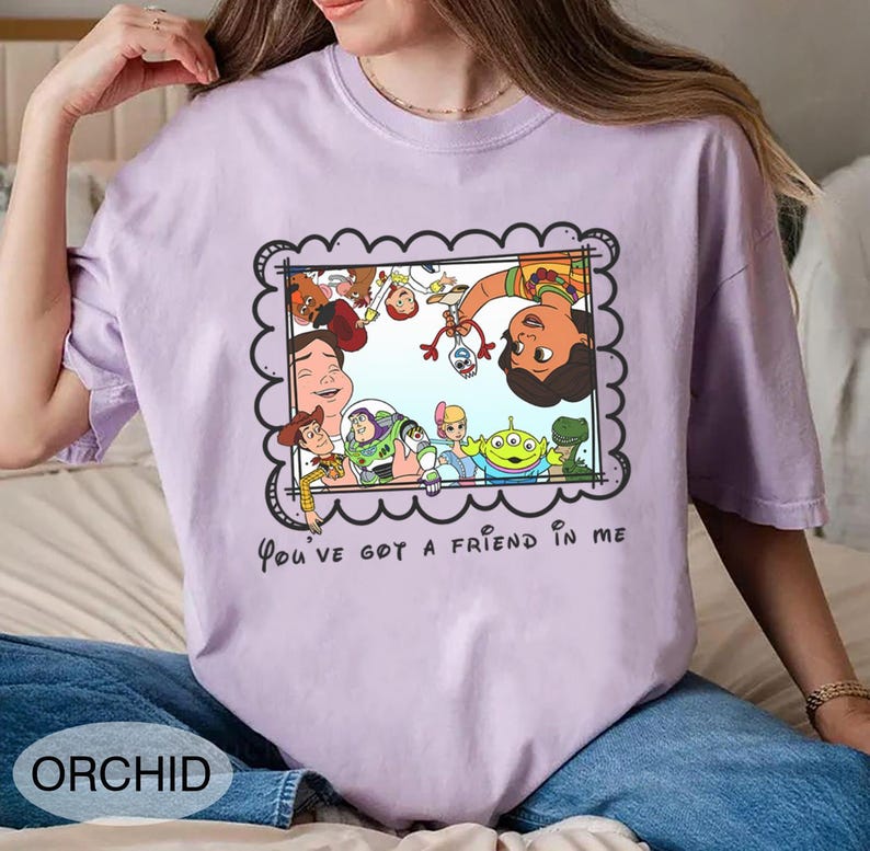 K&ouml;nnte beinhalten: Orchideenfarbenes T-Shirt mit einem gerahmten Cartoon-Bild von Charakteren aus dem Film Toy Story. Der Rahmen hat einen gewellten Rand, und der Text "You've got a friend in me" steht darunter. Das Wort "ORCHID" ist unten aufgedruckt.