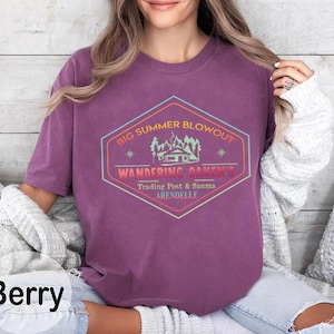 May include: Berry-colored t-shirt with a graphic that reads "Big Summer Blowout, Wandering Oaken's Trading Post & Sauma, Arendelle." The design is in a hexagon shape with a cabin and trees. The shirt is a crew neck.