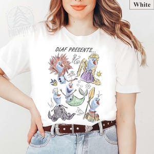 Puede incluir: Camiseta blanca con un gr&aacute;fico colorido de Olaf de Frozen con varios disfraces, incluyendo una sirena y una princesa. El texto "OLAF PRESENTS..." est&aacute; impreso encima de las ilustraciones. La camiseta est&aacute; hecha de un material suave.