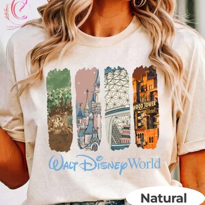 May include: A natural-colored t-shirt featuring four vertical rectangular designs with illustrations of Disney World landmarks. The words "Walt Disney World" are printed in blue script below the designs. The word "Natural" is printed in a white oval.