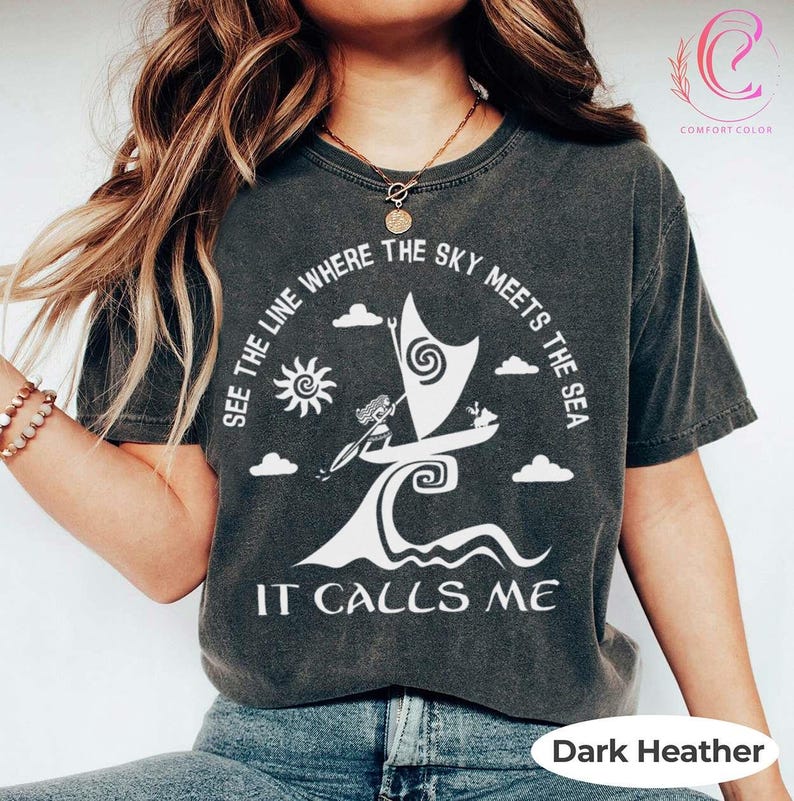 以下が含まれることがあります： ダークヘザーのComfort Colors Tシャツ。白いグラフィックは、太陽、雲、そして「SEE THE LINE WHERE THE SKY MEETS THE SEA IT CALLS ME」のテキストが入った、様式化されたヨットが特徴です。