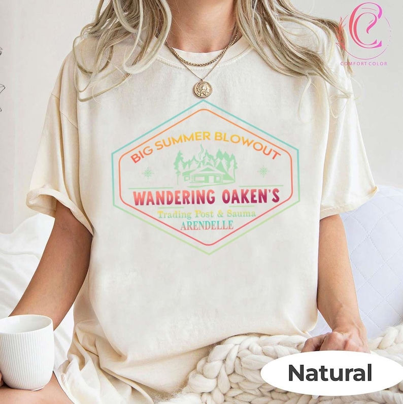 May include: Cream-colored t-shirt with a colorful graphic that reads "BIG SUMMER BLOWOUT" above "WANDERING OAKEN'S" and "Trading Post & Sauna ARENDELLE". The shirt is labeled "Natural" at the bottom right.