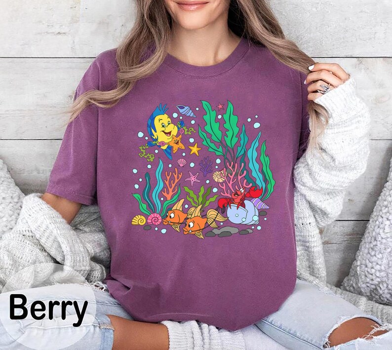 K&ouml;nnte beinhalten: Beerenfarbenes T-Shirt mit einer Cartoon-Grafik von Unterwasser-Meereslebewesen. Das Design umfasst Fische, eine Krabbe, Seetang und andere Meeresbewohner. Das Wort "Berry" ist unten in schwarzer Schrift gedruckt.