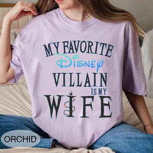 Peut inclure: T-shirt de couleur orchid&eacute;e avec l'inscription "MY FAVORITE Disney VILLAIN IS MY WIFE" dans une police stylis&eacute;e. Le mot "Disney" est en bleu et vert. Le t-shirt est &agrave; col rond.