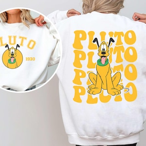 Könnte beinhalten: Weißer Pullover mit einem gelben Comic-Hund und dem Text "PLUTO EST. 1930" auf der Vorderseite. Die Rückseite des Pullovers hat das Wort "PLUTO" in einer gelben Retro-Schrift wiederholt.
