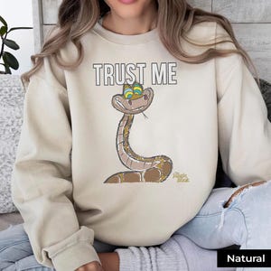 May include: A beige sweatshirt with the text "TRUST ME" and a cartoon snake from the Disney movie "The Jungle Book".