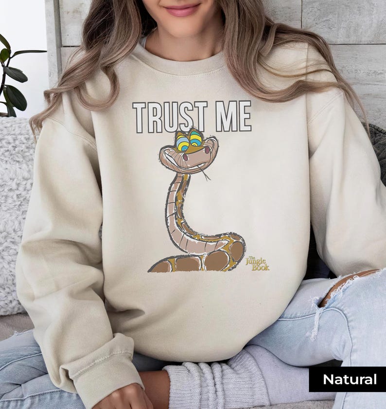 May include: A beige sweatshirt with the text "TRUST ME" and a cartoon snake from the Disney movie "The Jungle Book".