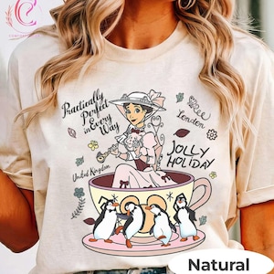 Puede incluir: Una camiseta de color crema con un gráfico de una mujer con vestido victoriano sentada en una taza de té grande, rodeada de cuatro pingüinos. El texto dice "Practically Perfect in Every Way", "London", "Jolly Holiday" y "United Kingdom".