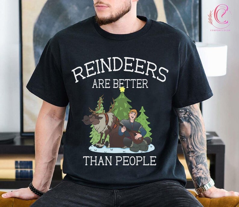 May include: Black t-shirt with the text "REINDEERS ARE BETTER THAN PEOPLE" in white. The graphic features a reindeer, a man playing a lute, and Christmas trees. The shirt is a crew neck.