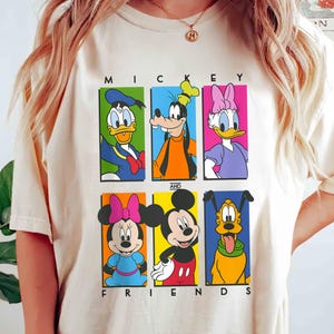 May include: A white t-shirt with a colorful graphic of Mickey Mouse and his friends. The graphic features Mickey Mouse, Minnie Mouse, Donald Duck, Goofy, Pluto, and Daisy Duck. The text "Mickey and Friends" is printed below the graphic.
